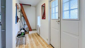 Een smalle gang met houten vloeren, een rode ladder die tegen de muur staat, een metalen karretje en een deur met geëtste glaspanelen.