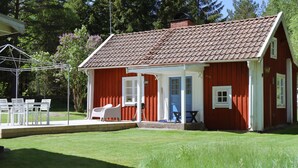 Een rode houten woning met een veranda, witte tuinmeubels en een gazon.
