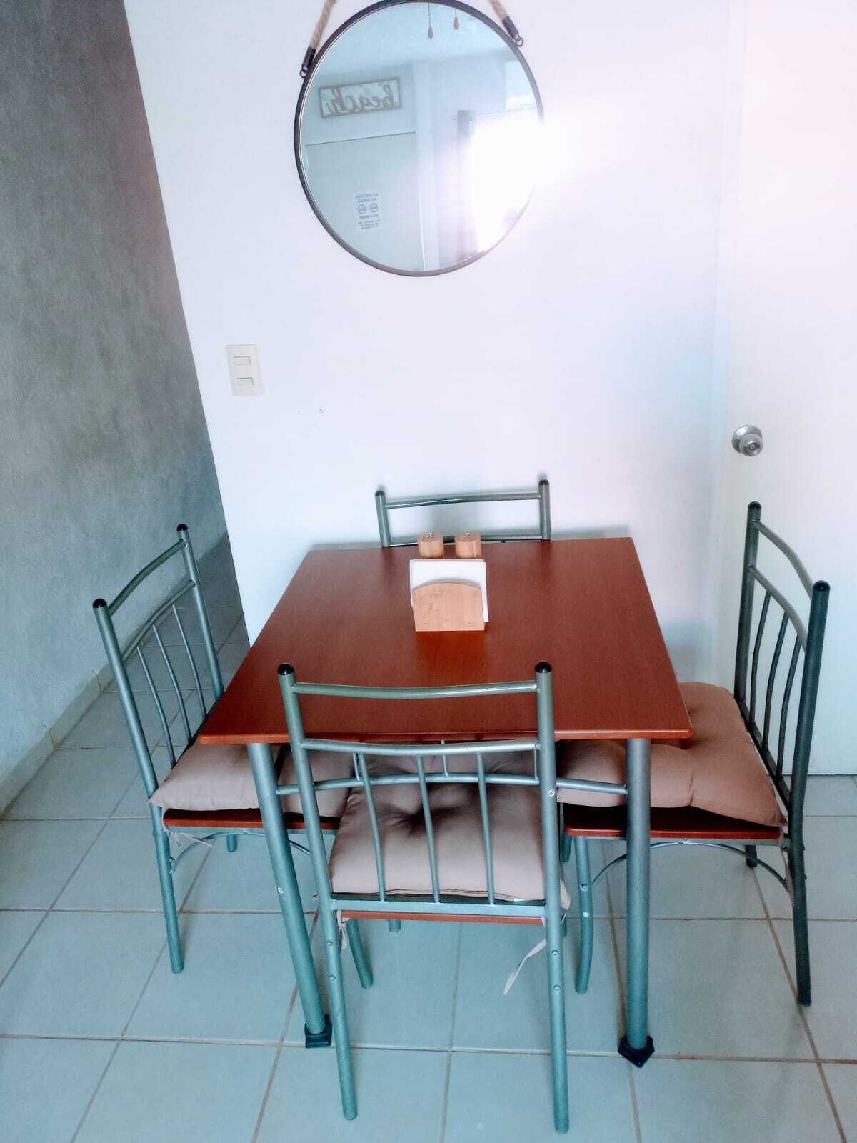 Een eettafel met vier stoelen, een ronde spiegel aan de muur en een deur met een knop.