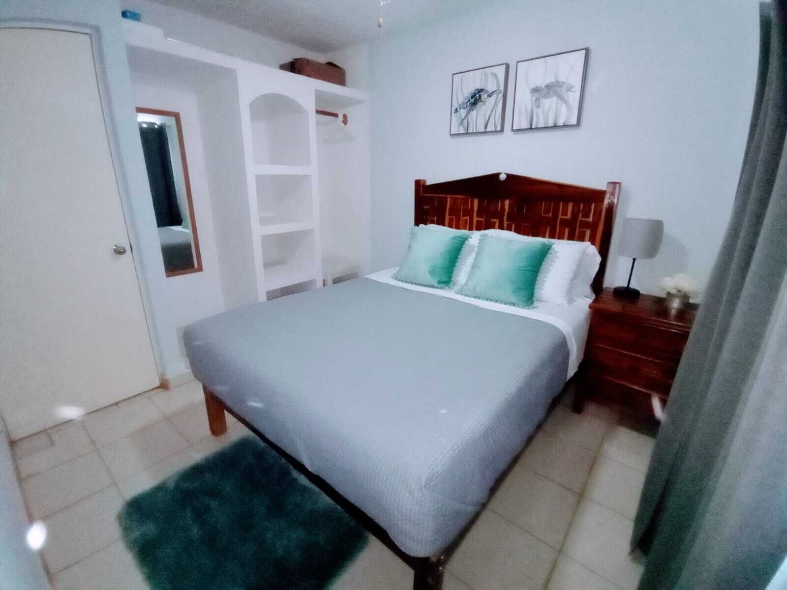 Een slaapkamer met een bed, nachtkastje, spiegel, kledingkast en twee decoratieve wandobjecten.