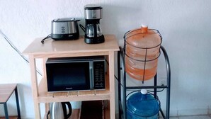 Een kitchenette met een magnetron, koffiezetapparaat, waterkoker en waterdispenser.