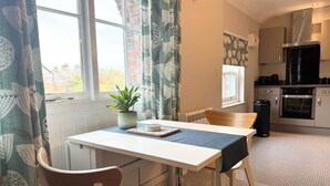 A dining area with a table, chairs, a potted plant, and a view of the kitchen. - Warehouse Apartments (Ulverston)
