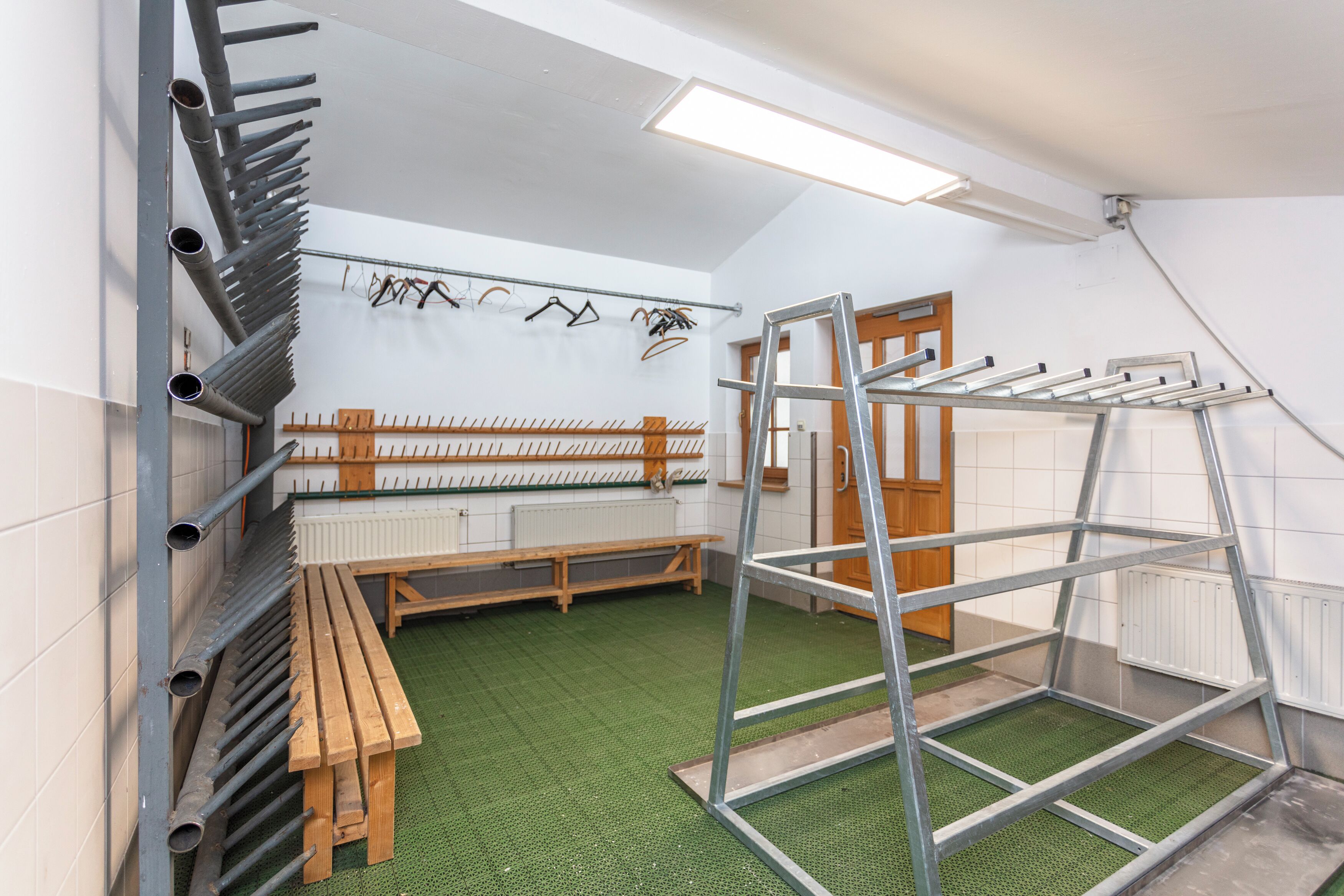 A room with a bench, a metal ladder, a wall-mounted rack with clothes, and a radiator.