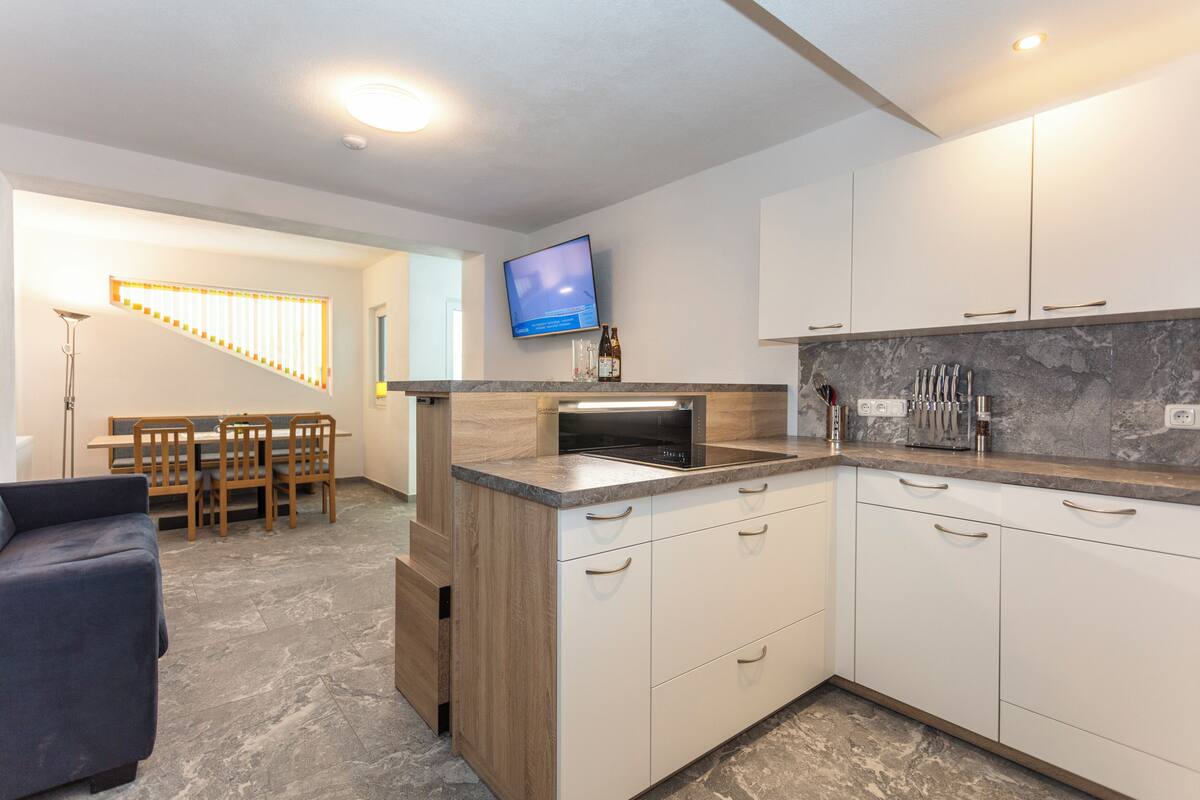 A modern kitchen with a built-in oven, a flat-screen TV, and a dining area with a wooden table and chairs.