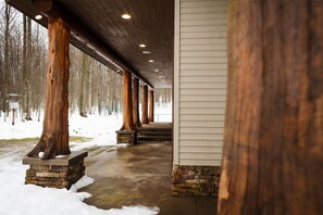 Un'area esterna coperta con colonne in legno e una base in pietra, che conduce a un edificio con rivestimento bianco.
