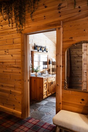 Interno di una baita in legno con angolo cottura, pavimento in pietra e tappeto a quadri.