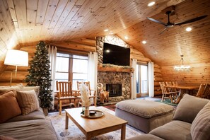 Accogliente interno di una baita in legno con camino, arredi in legno e albero di Natale.