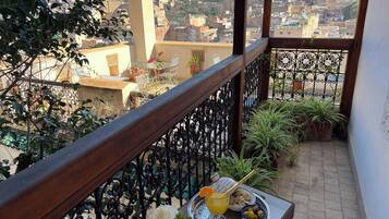 A balcony with a view of a cityscape, a table with a drink and snacks, and potted plants.