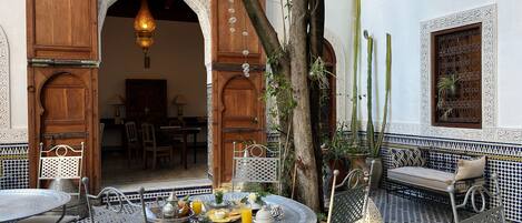 An outdoor dining area with a round table, chairs, and a variety of dishes and drinks.