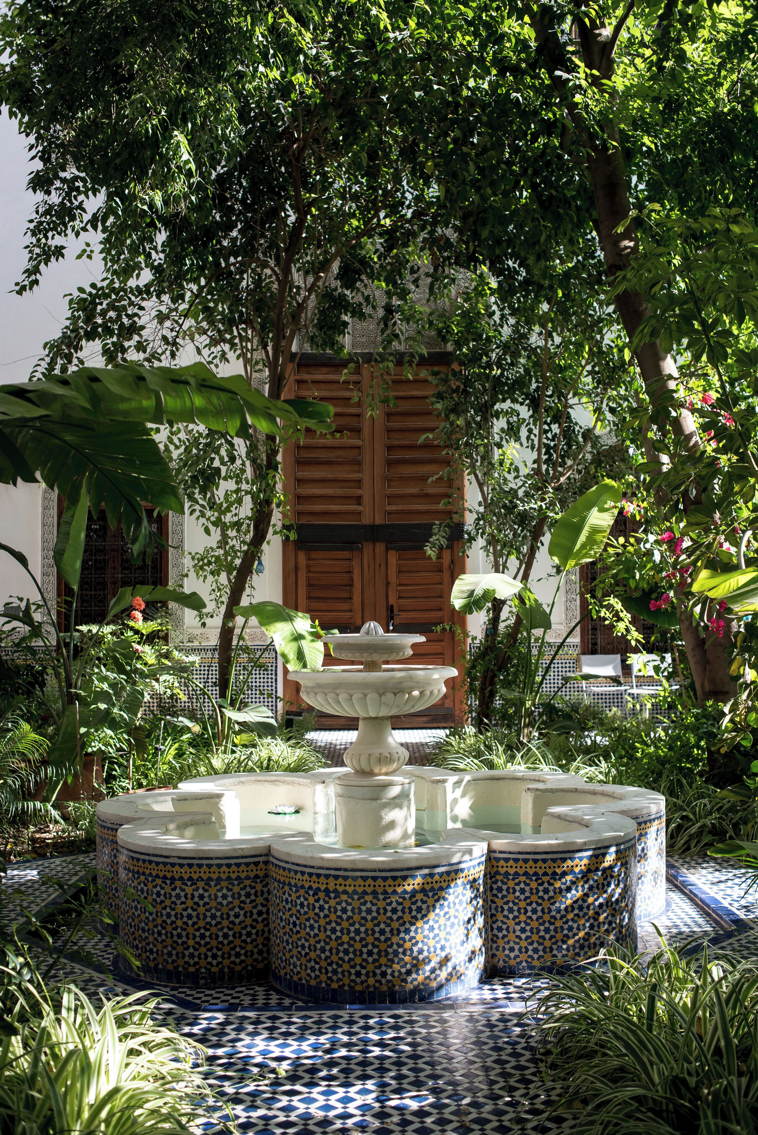 A courtyard with a fountain, tiled floor, and lush greenery.