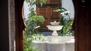 A traditional fountain with multiple tiers, surrounded by patterned tiles and lush greenery, viewed through an archway. - Riad Hanael Garden & Spa (Fès)