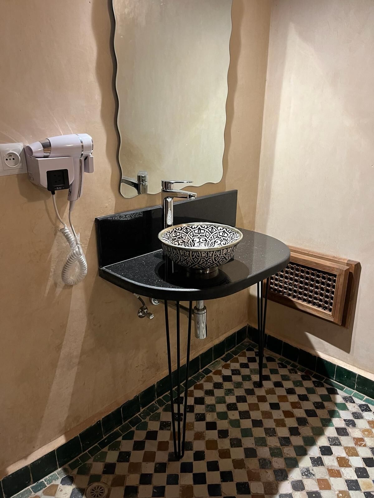 Een badkamer met een zwarte wastafel, een decoratieve kom, een haardroger en een ventilatierooster.