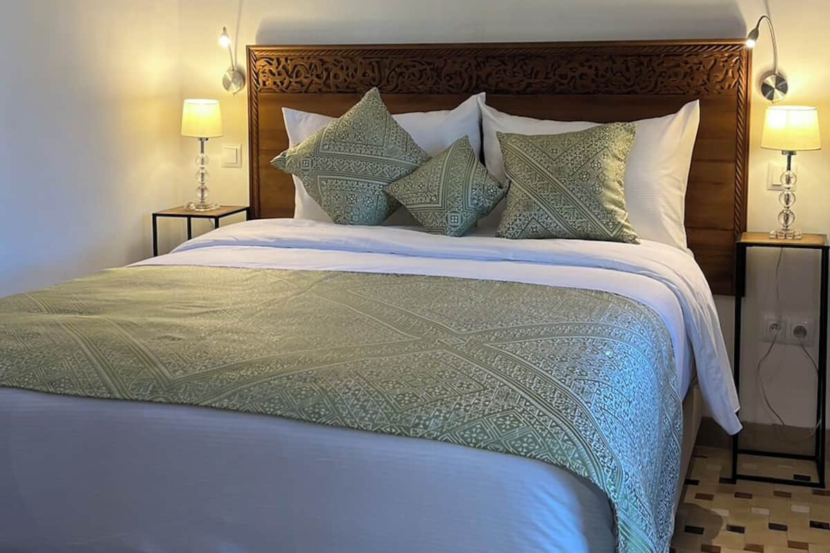 A neatly made bed with patterned bedding and pillows, two bedside lamps, and a decorative ceiling medallion.