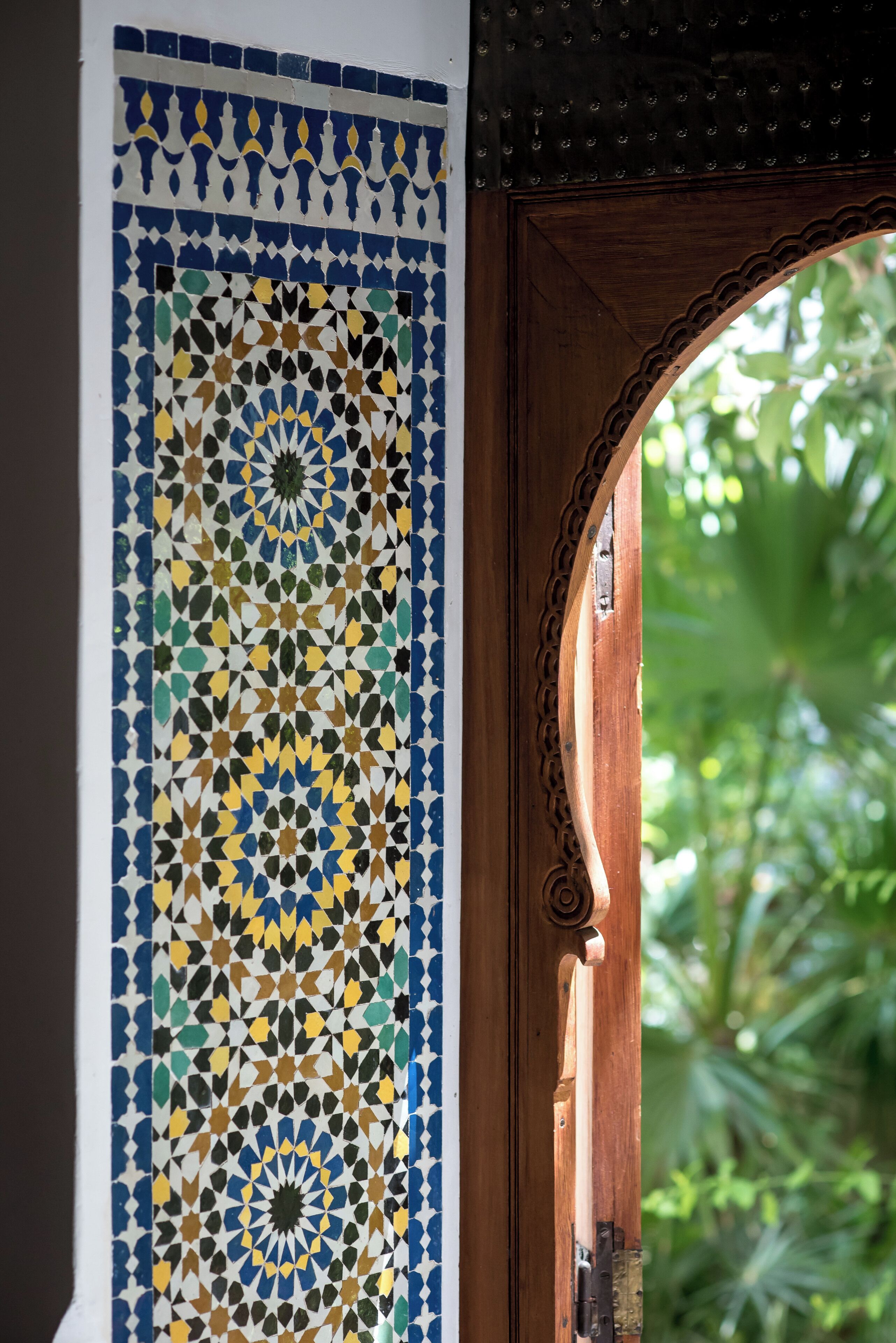A wooden door with a decorative tile pattern and an archway leading to a garden.