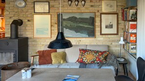 Una sala de estar acogedora con chimenea, un sofá con cojines de colores, una mesa con un libro y una estantería llena de libros.
