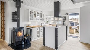 A modern kitchen with a central island, white cabinetry, and a wood-burning stove. - Pet friendly home in Blokhus with WiFi (Blokhus)