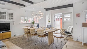 A modern dining area with a wooden table and chairs, a chandelier, and a television in the background. - Pet friendly home in Blokhus with WiFi (Blokhus)