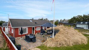 A red house with a tiled roof, a patio with outdoor furniture, and a large pile of hay. - Pet friendly home in Blokhus with WiFi (Blokhus)