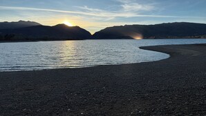 Rauhallinen järvi, taustalla kohoavat vuoret ja auringonlasku veden yllä – täydellinen ranta.
