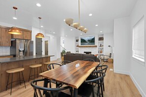 Une cuisine moderne avec des meubles en bois, des appareils électroménagers en acier inoxydable et une table à manger en bois, accompagnée de tabourets de bar.