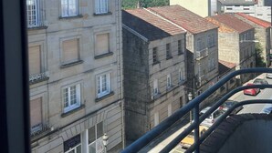 Vista de un edificio con varios pisos y balcones, cielo azul despejado y una calle con coches estacionados.