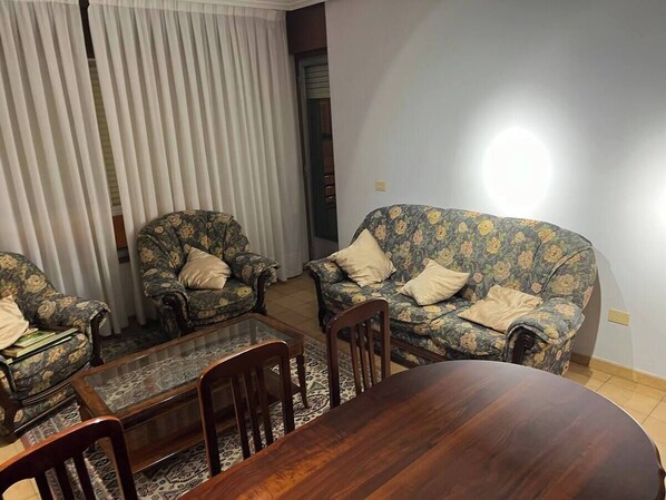 Een woonkamer met een houten eettafel, twee banken met bloemenprint en bijpassende fauteuils.