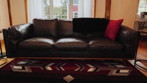 Un sofá de cuero marrón con un cojín rojo en una habitación con vigas de madera y una alfombra estampada.