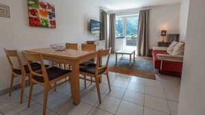 Een eethoek met een houten tafel en stoelen, een televisie en een rode bank.