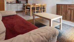 Een woonkamer met een rode bank, een houten eettafel met stoelen, een keuken en een houten kast.