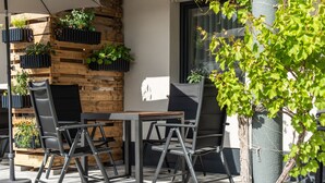 Een terras met een houten wand, metalen stoelen en plantenpotten.