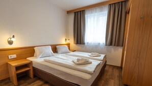 A hotel room with two beds, wooden headboards, a nightstand, a wardrobe, and a window with curtains.