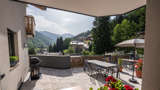 An outdoor patio with a table and chairs, a grill, and potted plants. - Appartement MaLo - Top 3 (Viehhofen)