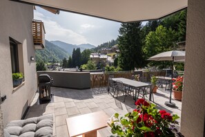 An outdoor patio with a table and chairs, a grill, and potted plants. - Appartement MaLo - Top 3 (Viehhofen)