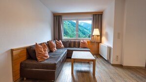 A modern living room with a sectional sofa, a wooden coffee table, and a view of a mountainous landscape through a large window. - Appartement MaLo - Top 3 (Viehhofen)