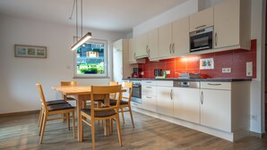 A modern kitchen with wooden dining table and chairs, white cabinets, and a red backsplash. - Appartement MaLo - Top 3 (Viehhofen)