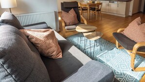 A modern living room with a sofa, armchair, and coffee table, a dining area with a table and chairs, and a kitchen in the background.