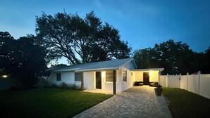 A single-story house with a paved driveway leading to a front door, surrounded by a white fence and a well-maintained lawn. - Charming 3‑BR Sarasota Retreat — Minutes to Beaches & Downtown (Sarasota)