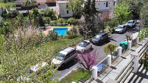 Un quartier résidentiel avec une piscine, des voitures garées et une colline en arrière-plan, sur laquelle se trouvent des bâtiments.