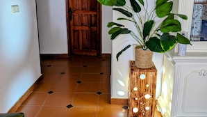 Un couloir avec une porte en bois portant l’inscription «Toilettes», une plante en pot et un sol carrelé.