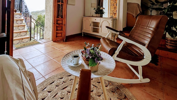 Un salon spacieux avec une grande fenêtre, une table à manger avec une tasse de café, un canapé et un fauteuil.