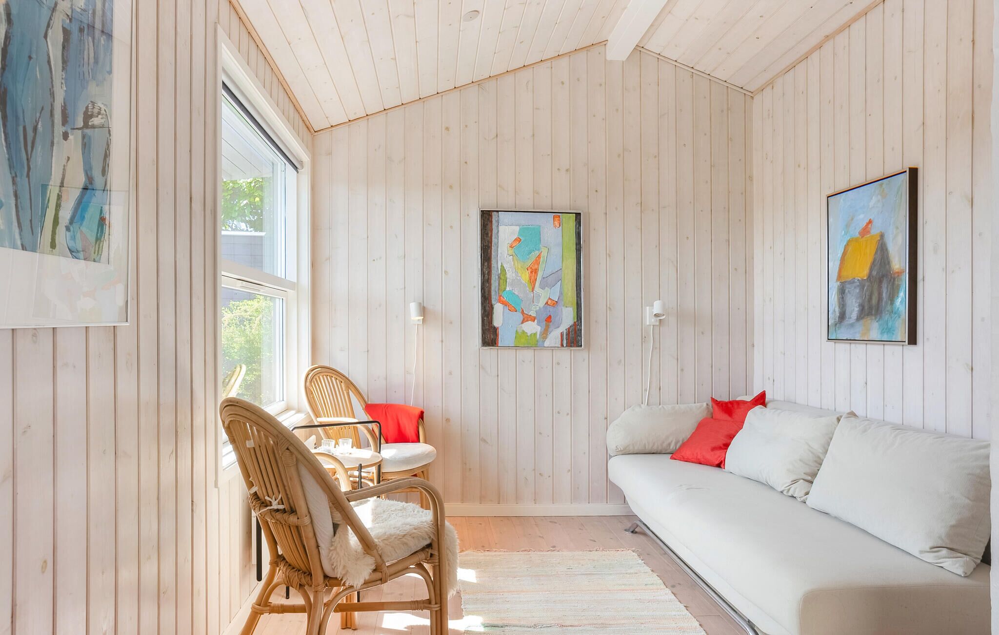 Um quarto aconchegante com um sofá branco, uma mesa de jantar com cadeiras e duas pinturas abstratas nas paredes.