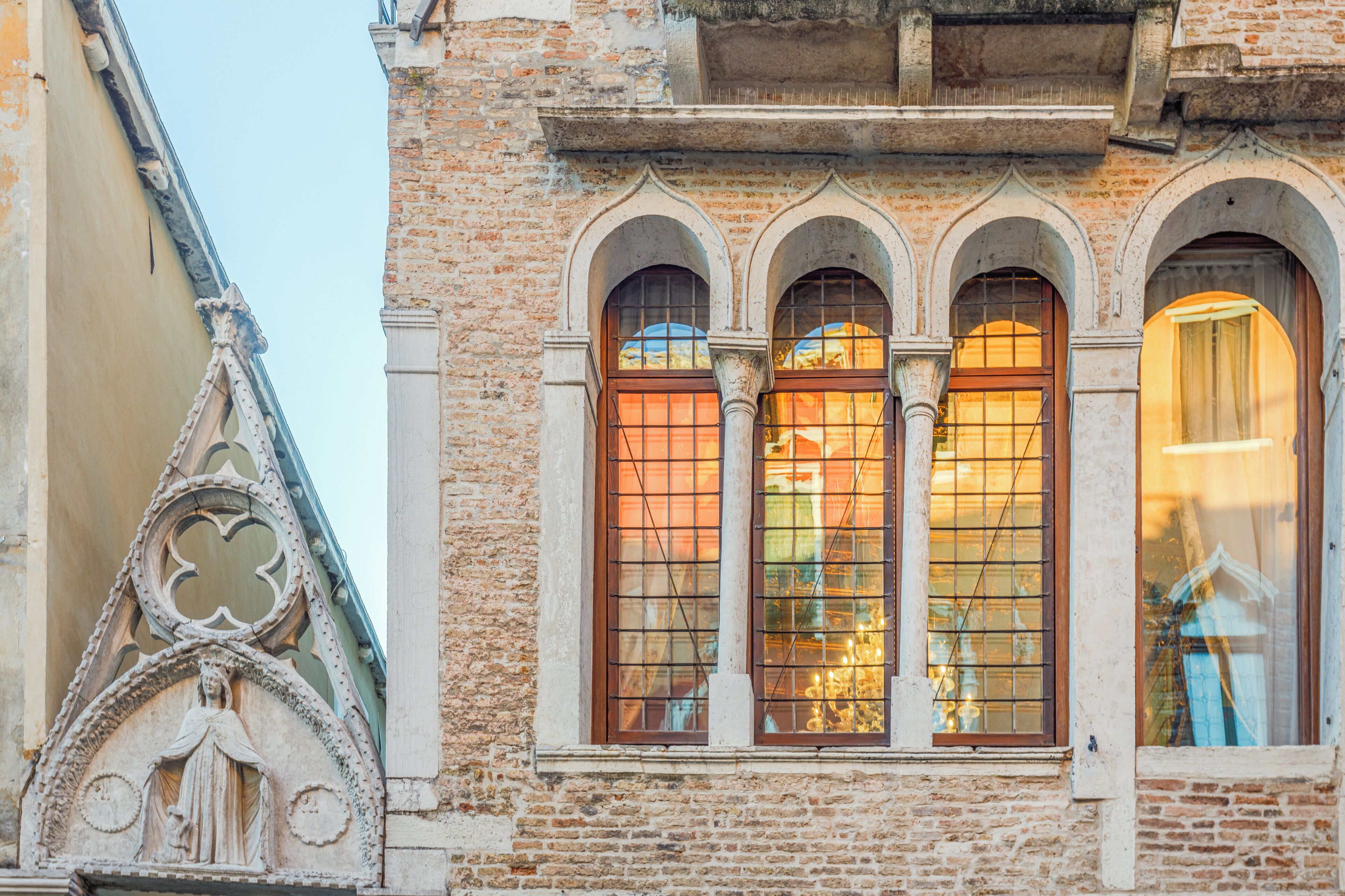 Fachada d'edifici amb tres finestres d'arc i una decorativa talla de pedra.