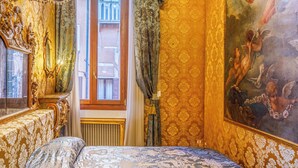 A luxurious bedroom with ornate gold wallpaper, a large bed with a detailed patterned bedspread, a chandelier, and a mural on the wall. - Canal View San Marco Rialto -Dogaressa Palace 1872 (Venezia)