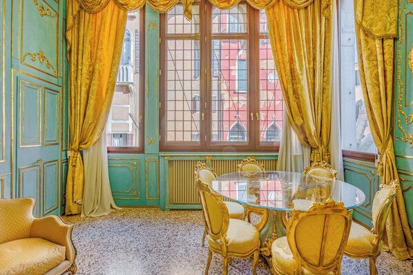 A room with a round glass table and four chairs, a sofa, and a window with curtains.