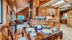 A wooden cabin interior with a dining area set for a meal, a kitchen with wooden cabinets, and a cozy living space with a fireplace.