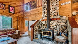 A cozy cabin interior with a stone fireplace, wooden walls, a sofa, and a dining table.