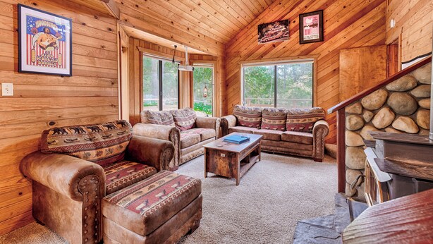 A log cabin interior with wooden walls, a stone fireplace, and a large window.