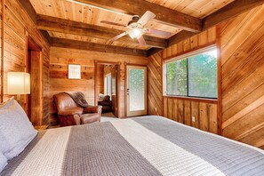 Ein Schlafzimmer einer Holzhütte mit Bett, Stuhl, Deckenventilator und Fenster.