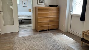 A bedroom with a wooden dresser, a bed, a window with a view, and a door leading to another room. - Spacious and quiet  1-bedroom  place in Munich. Fully equipped sleeps 7 guests! (Munich)