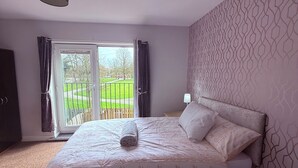 Une chambre avec un grand lit, une vue sur un jardin accessible par une porte coulissante et un mur décoré d’un motif.